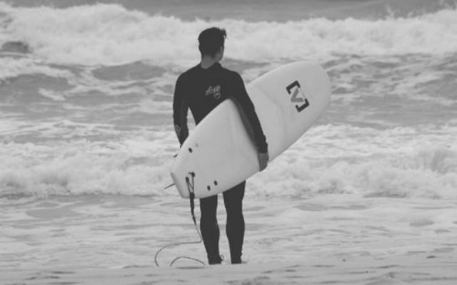 Surfer steht am Strand und blickt aufs Meer