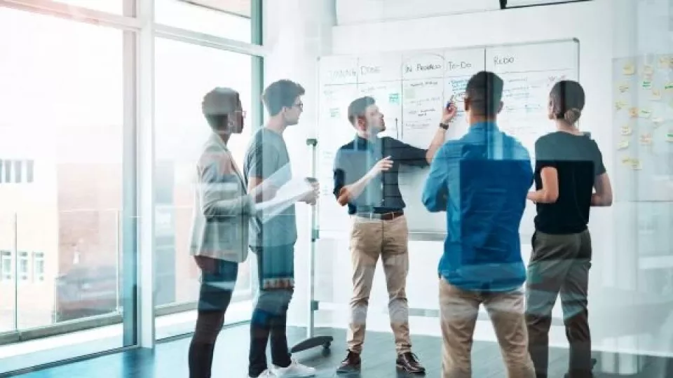 Gruppen von Geschäftsleuten in einem modernen Büro, die an einem Flipchart stehen und gemeinsam eine operative Vertriebsstrategie entwickeln. Die Personen diskutieren aktiv, um ihre Vertriebsplanung zu optimieren und erfolgreich umzusetzen.