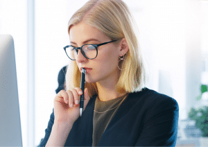 Eine junge Frau hält einen Stift an die Lippen und wirkt nachdenklich und unschlüssig.