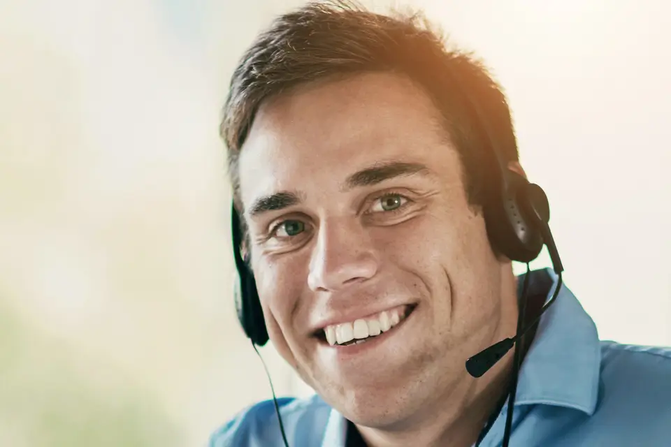 Mitarbeiter mit Headset blickt freundlich in die Kamera und bereitet sich auf ein Telefonakquise-Gespräch vor.