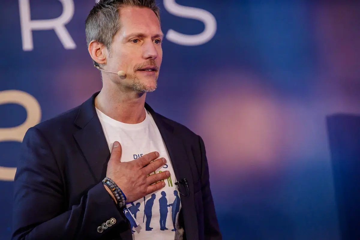 Dirk Stöcker auf der Bühne beim Vortrag über emotionales und werteorientiertes Verkaufen, mit Hand aufs Herz als starkes Zeichen für ehrliche Kundenbeziehung.