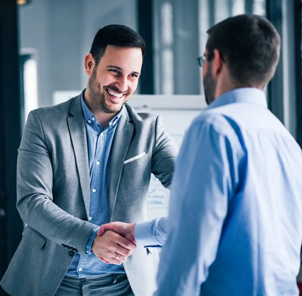 Zwei Geschäftspartner beim Handschlag nach einer punktgenauen Bedarfsanalyse und einem Verkaufsgespräch auf Augenhöhe.