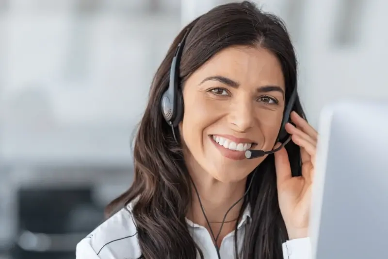 Freundliche Frau mit Headset telefoniert lächelnd in einem modernen Büro, symbolisiert Telefonakquise im Kundenservice.