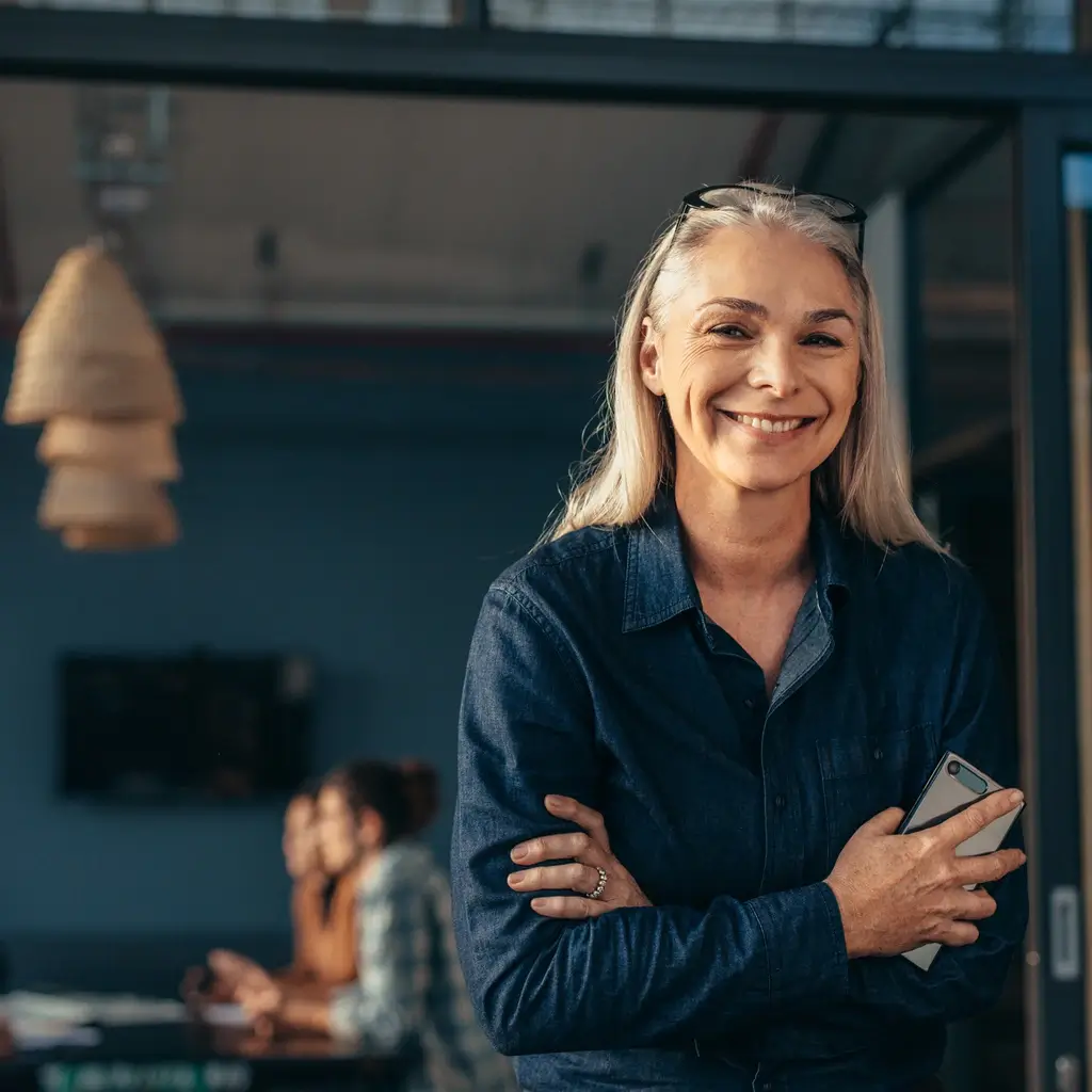 Eine lächelnde HR-Mitarbeiterin im Fokus, während im Hintergrund ein motiviertes Team gemeinsam arbeitet.
