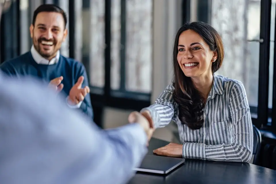 Verkäuferin gibt ihrem Kunden lächelnd die Hand nach einem erfolgreichen Verkaufsgespräch
